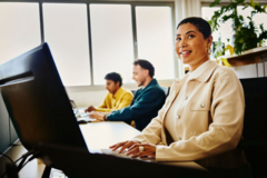 una donna sorridente e alcuni colleghi che lavorano al pc in ufficio