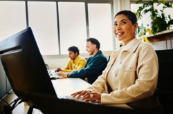 una donna sorridente e alcuni colleghi che lavorano al pc in ufficio