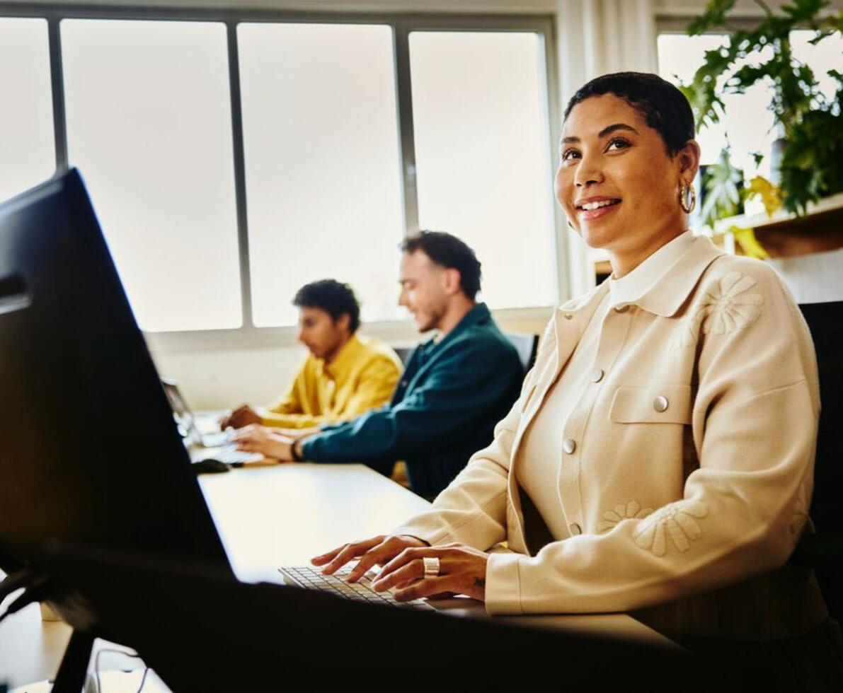 una donna sorridente e alcuni colleghi che lavorano al pc in ufficio
