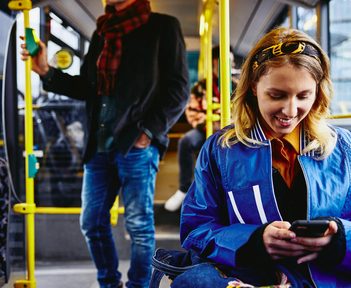 una ragazza sorridente che scrive al telefono seduta su un autobus