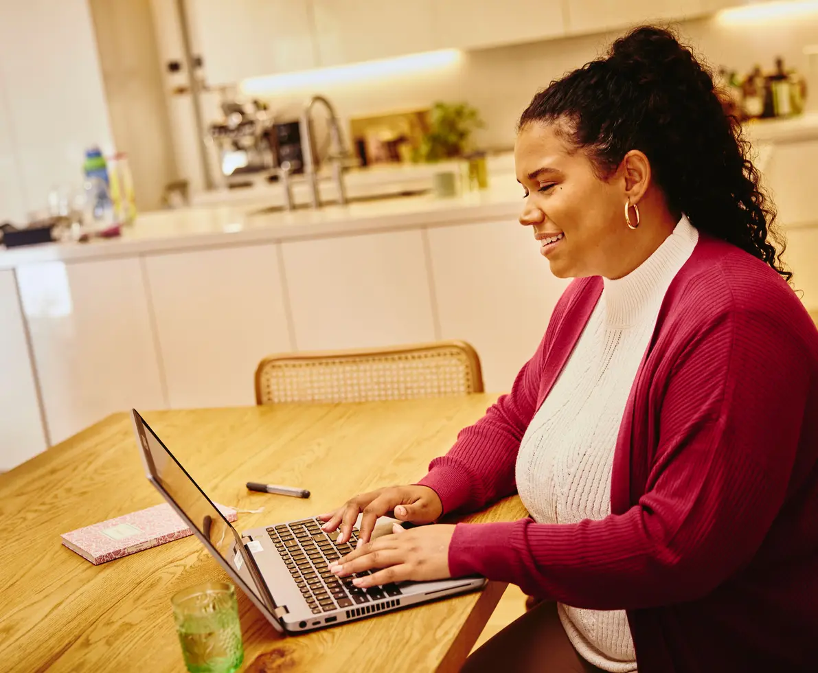 una donna che lavora al pc seduta ad un tavolo nella cucina di casa