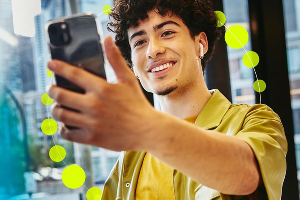 un ragazzo sorridente in primo piano che si inquadra tenendo in mano un cellulare