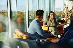 un gruppo di colleghi che parla seduto su delle poltrone in una sala finestrata - team building aziendale