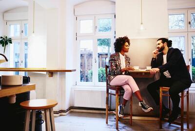 due ragazzi seduti ad un tavolo in un ambiente informale che parlano mentre prendono un caffe - people management