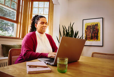 una donna che lavora al suo pc seduta ad un tavolo nel salotto di casa