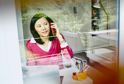 una donna al telefono seduta ad una scrivani davanti ad una finestra