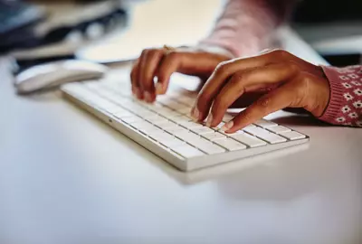 due mani che scrivono su una tastiera bianca