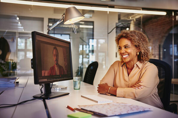una donna sorridente seduta ad una scrivania che parla in videoconferenza con un collega 